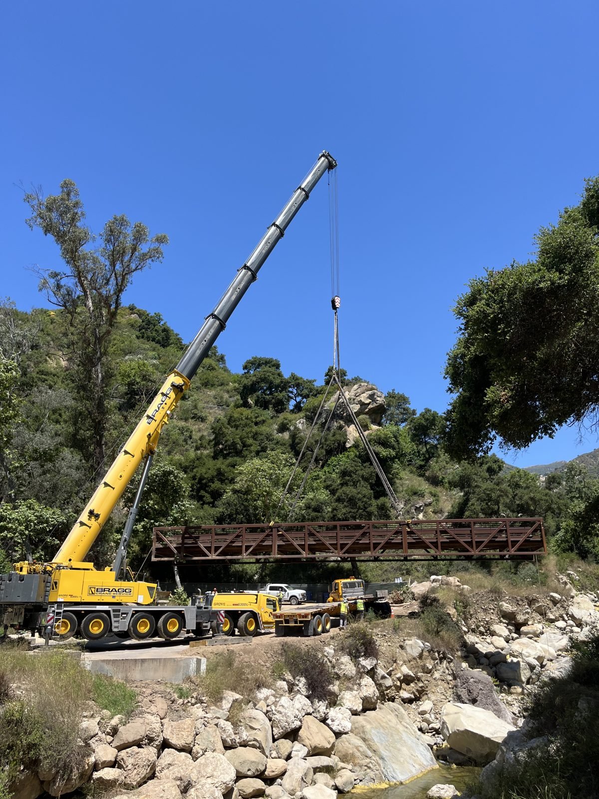 Crane lifting a full steel truss bridge span out of a rocky creek canyon